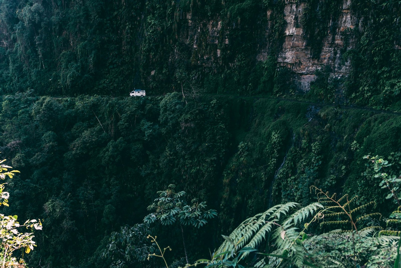 An adrenaline-fueled car zooming down the breathtaking and treacherous yungas road in bolivia, surrounded by lush greenery and towering mountains.