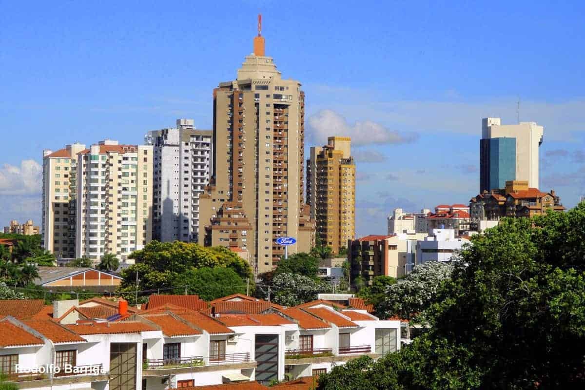 A vibrant urban skyline of santa cruz de la sierra showcases its dynamic energy, featuring modern architecture and bustling shopping centers, with a glimpse of parque el arenal and its serene water features in the foreground